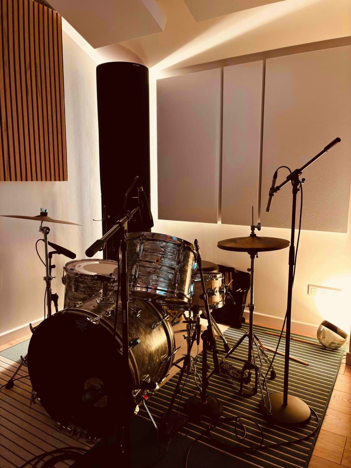 Batterie acoustique installée dans la salle de prise de son, entourée de panneaux acoustiques et de pieds de micro