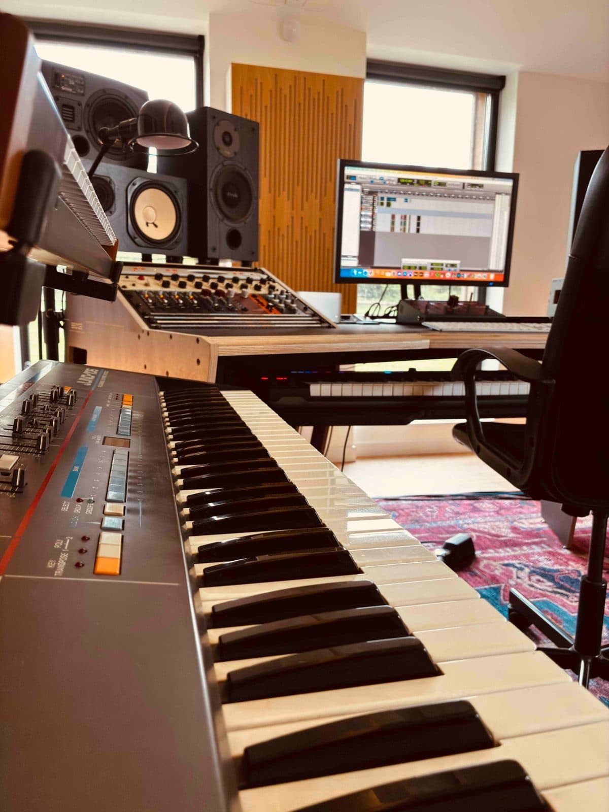 Clavier de synthétiseur Roland Juno au premier plan, devant le bureau de la régie, les enceintes de monitoring et l'écran de la station audio