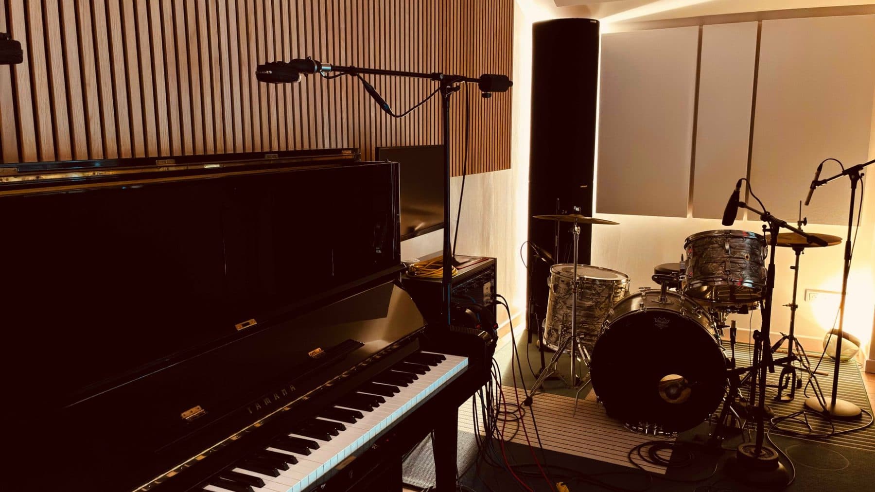 La salle de prise de son : piano droit Yamaha et batterie devant des panneaux acoustiques en bois