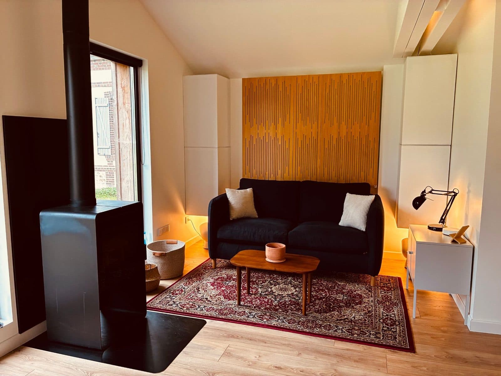 L'espace détente : canapé, poêle à bois et mur acoustique en bois, éclairés d'une lumière chaude